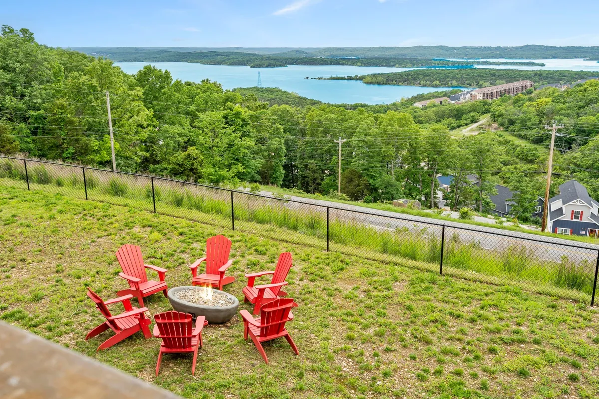 Red Adirondack chairs circle a firepit overlooking the lake, surrounded by lush greenery. The scene is perfect for evening gatherings, stargazing, or watching the sunset, with the serene water creating a peaceful backdrop.