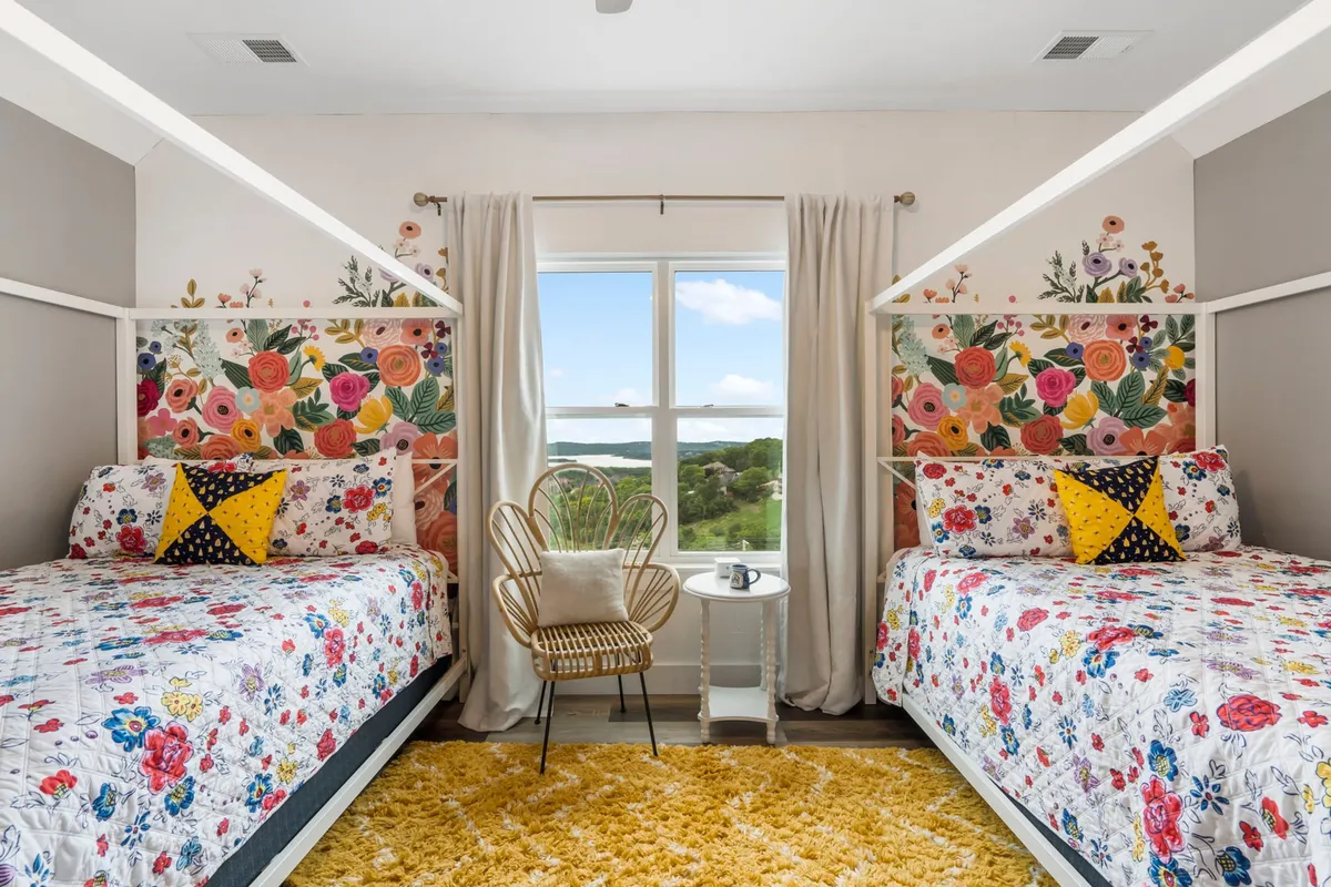 A playful and cozy bunk room with colorful floral wallpaper, two bunk beds with floral bedding, a golden rug, and a stylish seating area. The space feels lively yet comfortable, ideal for kids or groups wanting a special hideaway.