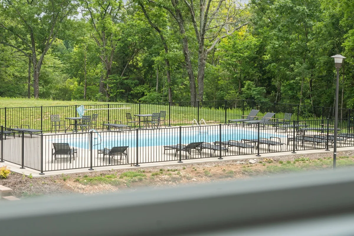 A close-up of the resort-style swimming pool, surrounded by lounge chairs and lush greenery, with a fence ensuring privacy and safety. The inviting pool area is calm and uncrowded—matching the description of boutique shared amenities.