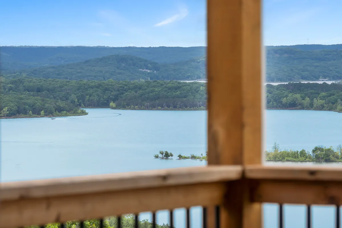 A sweeping view of Table Rock Lake framed by lush trees and distant mountains under a bright blue sky. The lake's inviting waters and natural shoreline suggest opportunities for boating, fishing, and exploring. The peaceful atmosphere highlights the lake's scenic beauty and outdoor recreational appeal.