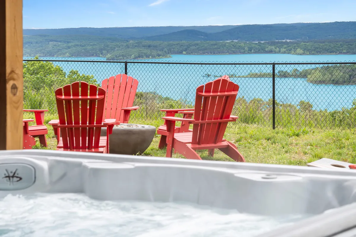 A relaxing lakeside setup featuring a hot tub, red Adirondack chairs, and a captivating view of the lake. The area is inviting for unwinding after a day on the water, with seating oriented toward scenic vistas and the tranquil water below.