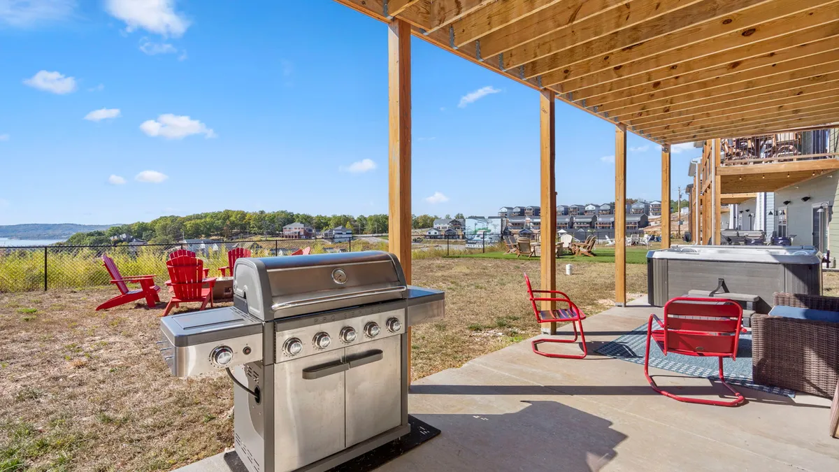 This exterior image displays a grill, red chairs, a hot tub, and a sweeping view of the lake. The arrangement suggests outdoor dining, relaxation, and group enjoyment in a beautiful setting.