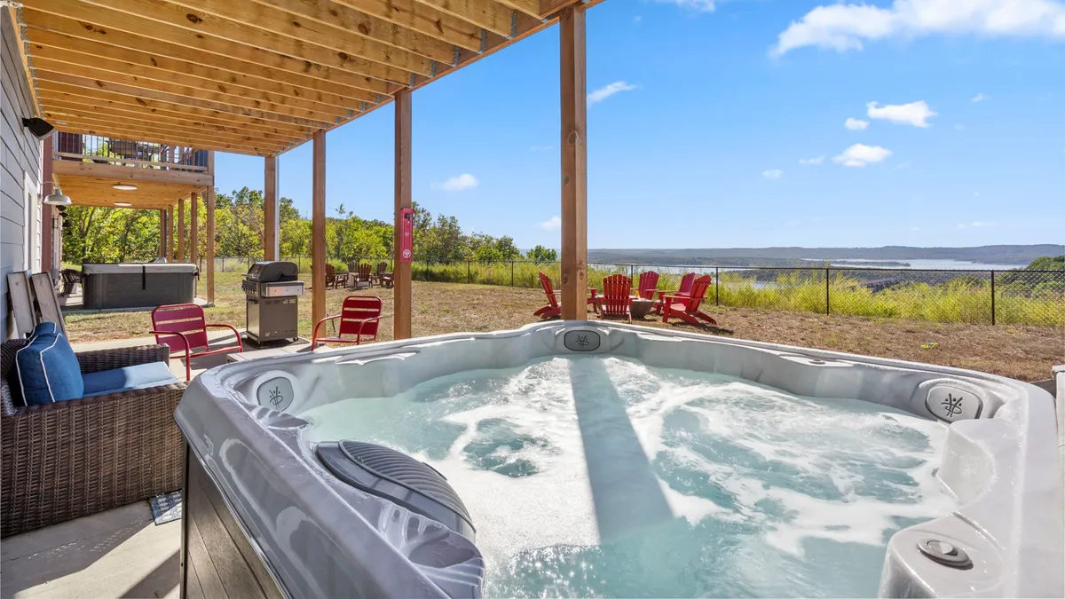 This exterior image features a hot tub with outdoor seating, set against a scenic landscape backdrop. The view extends beyond the seating area, inviting guests to relax, socialize, and enjoy the peaceful surroundings.