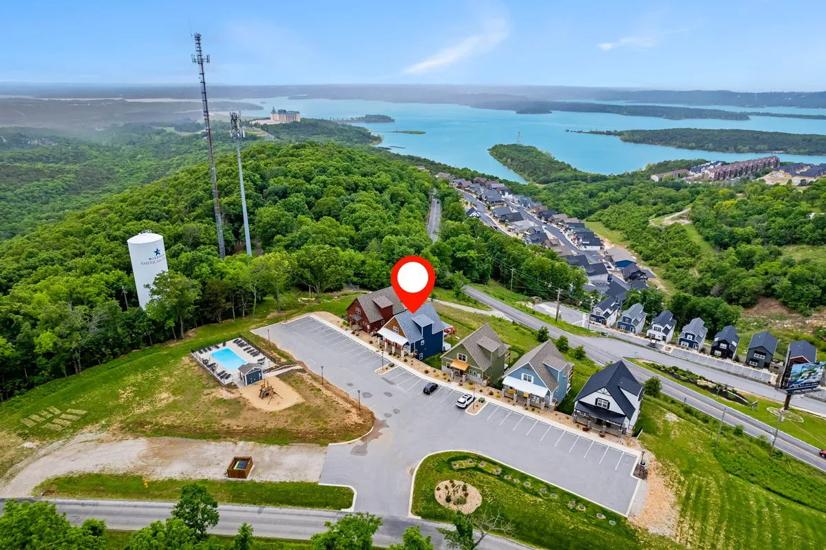 A wide-angle exterior shot features the shimmering swimming pool, playful playground area, and a stunning view of the lake, all set against the backdrop of colorful homes and vibrant greenery. The image exudes a sense of relaxation and adventure with the pool and playground in the foreground and the lake just beyond.