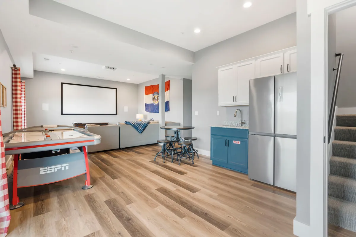 A lively entertainment space with an air hockey table, comfortable seating area, kitchenette with bar stools, and a wall-mounted TV. The room is designed for fun, games, and easy access to snacks and drinks.