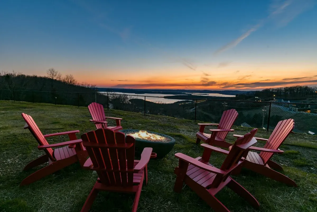 The hero image features a cozy group of red Adirondack chairs circling a crackling fire pit, set against a stunning sunset backdrop overlooking Table Rock Lake. The tranquil scene invites guests to gather, converse, enjoy nature, and take in the breathtaking views as day turns to night.