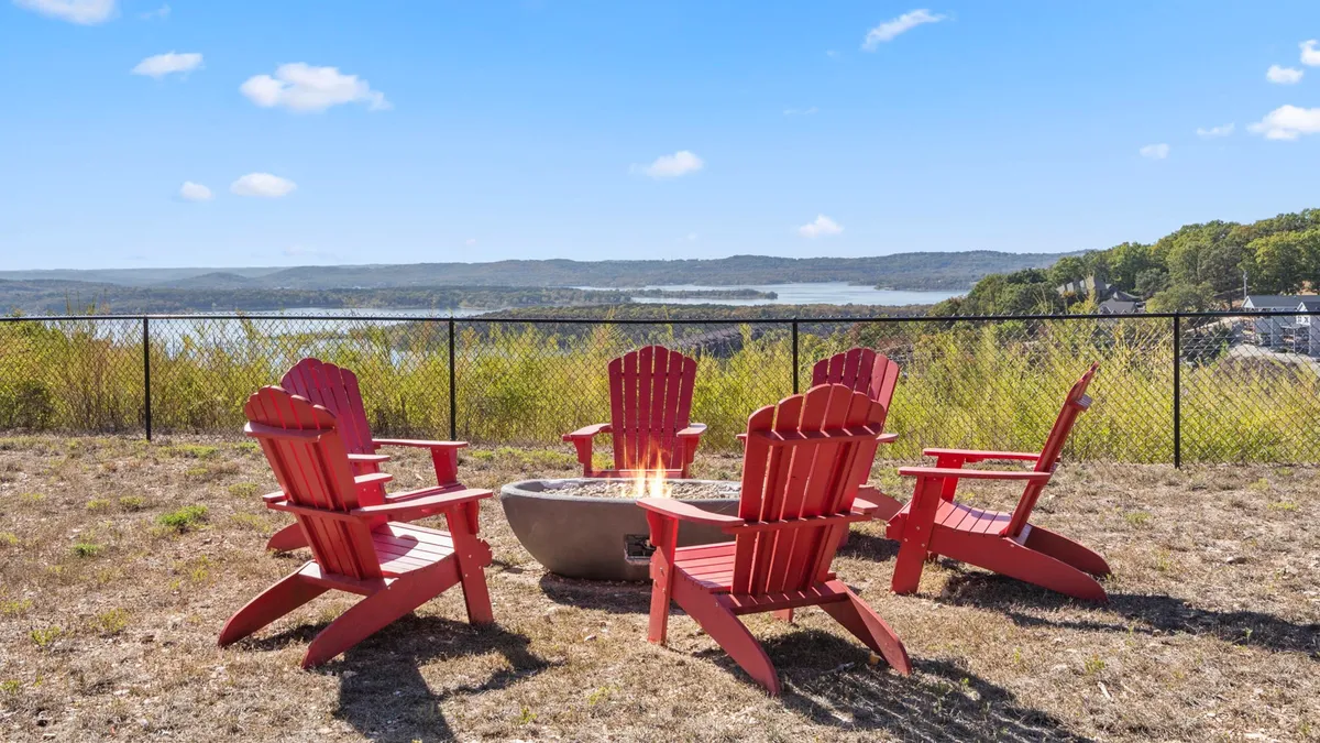 This exterior image showcases red Adirondack chairs arranged around a fire pit, overlooking the lake. The cozy setting highlights opportunities for storytelling, lakeside gatherings, and enjoying nature in a small-community environment.